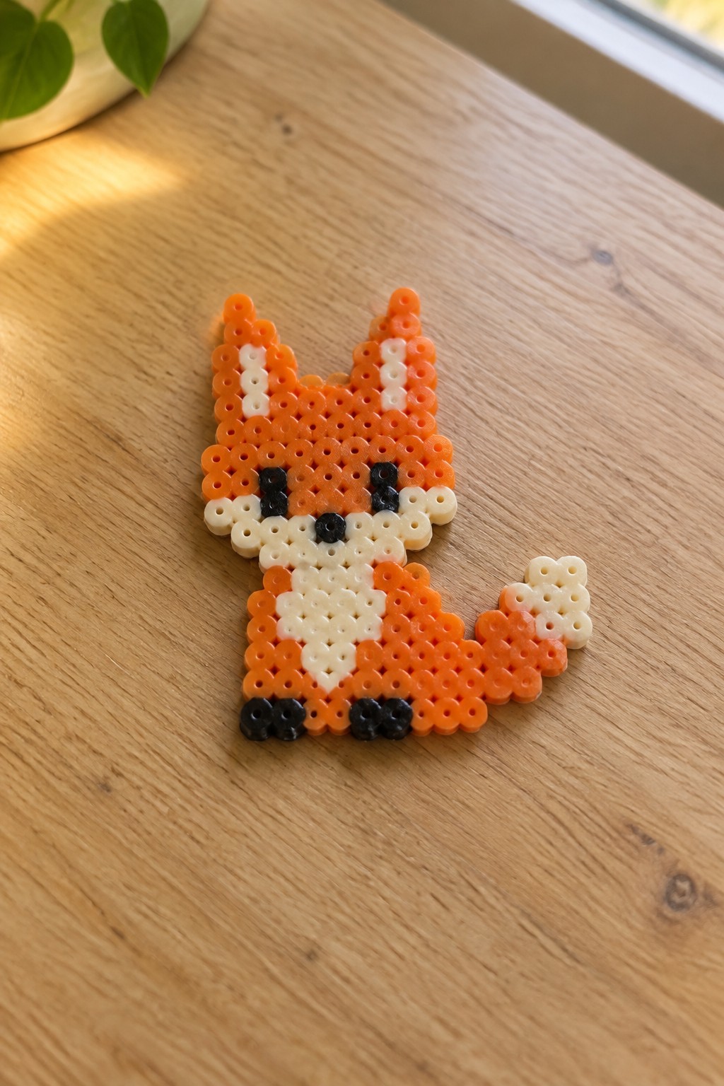 Orange perler bead fox with white chest, black eyes, and feet on wood