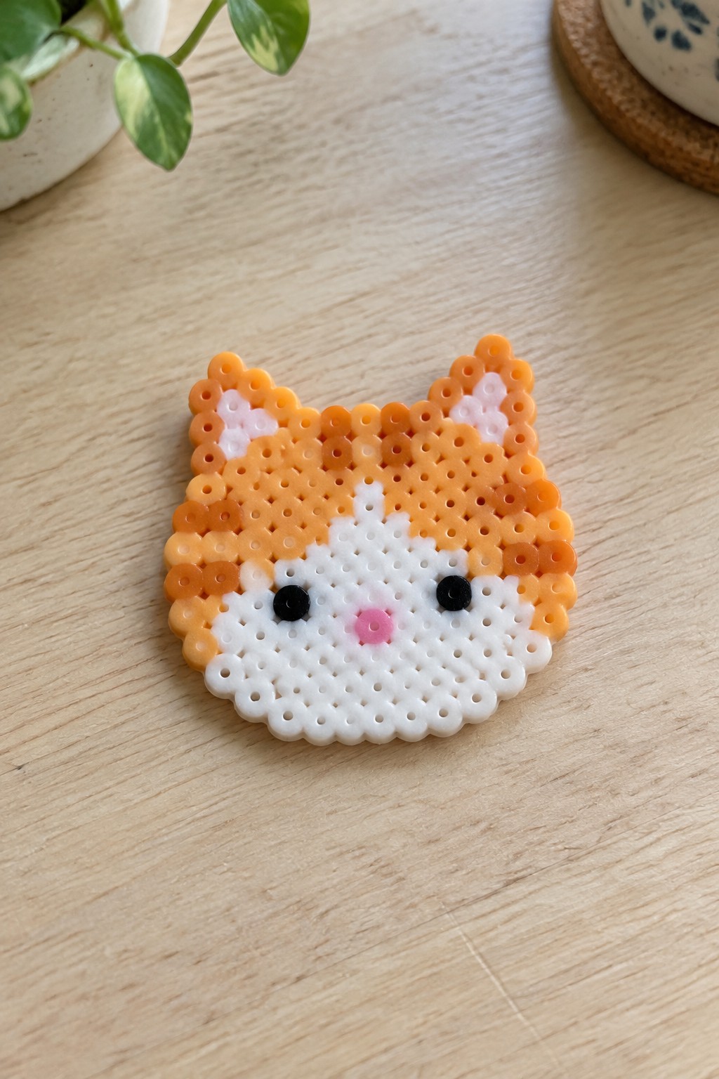 Orange and white Perler bead cat face arranged on a pegboard.