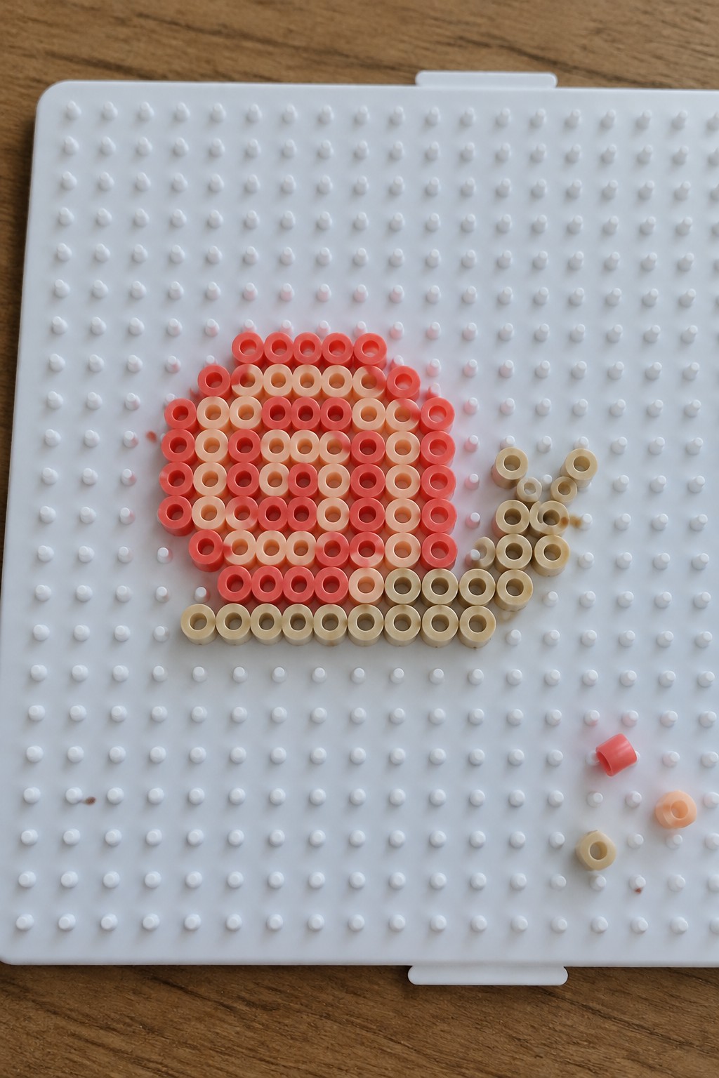 Gradient pink and beige beads forming a teapot on white pegboard