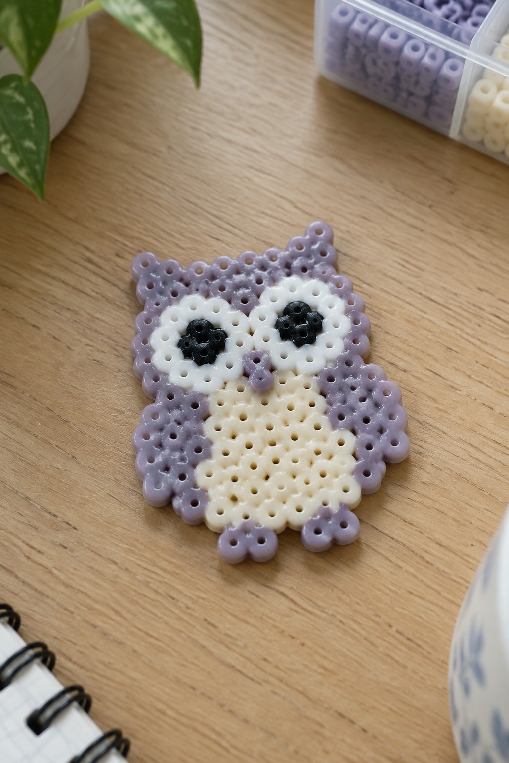 Perler bead owl in purple, white, black, and cream on wooden table