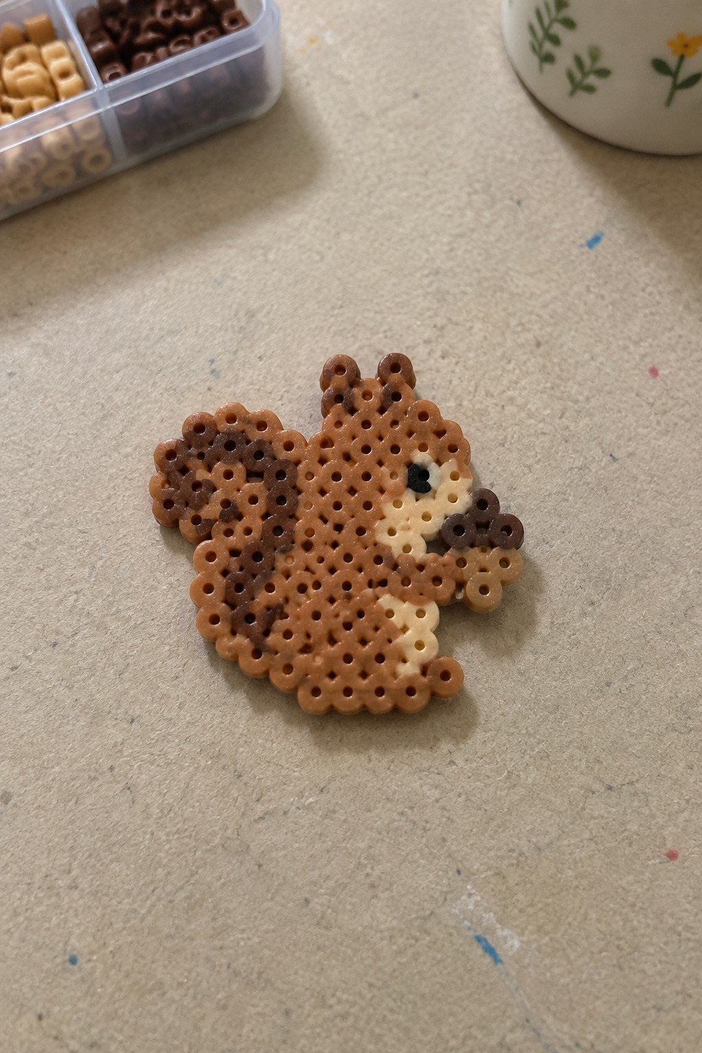 Mini Perler bead squirrel made with brown, tan, and dark brown beads on a pegboard.
