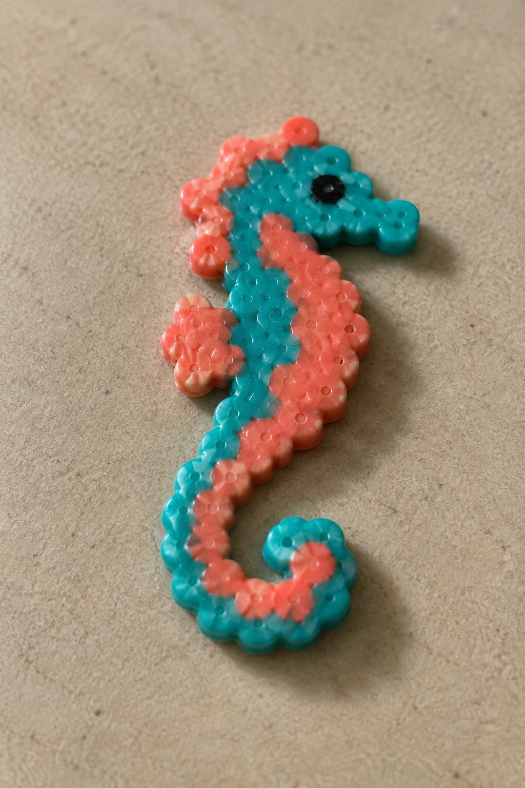 Pink and turquoise beaded seahorse with black eye on beige surface