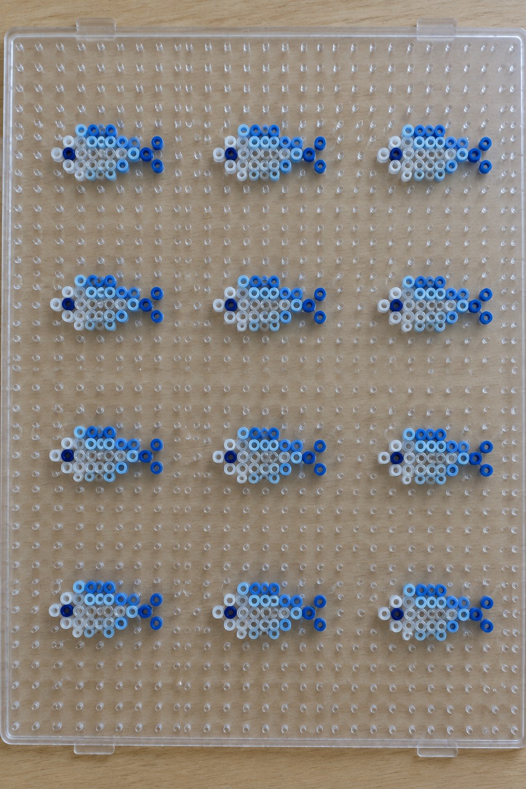 Twelve blue and white beaded fish designs on a clear pegboard.