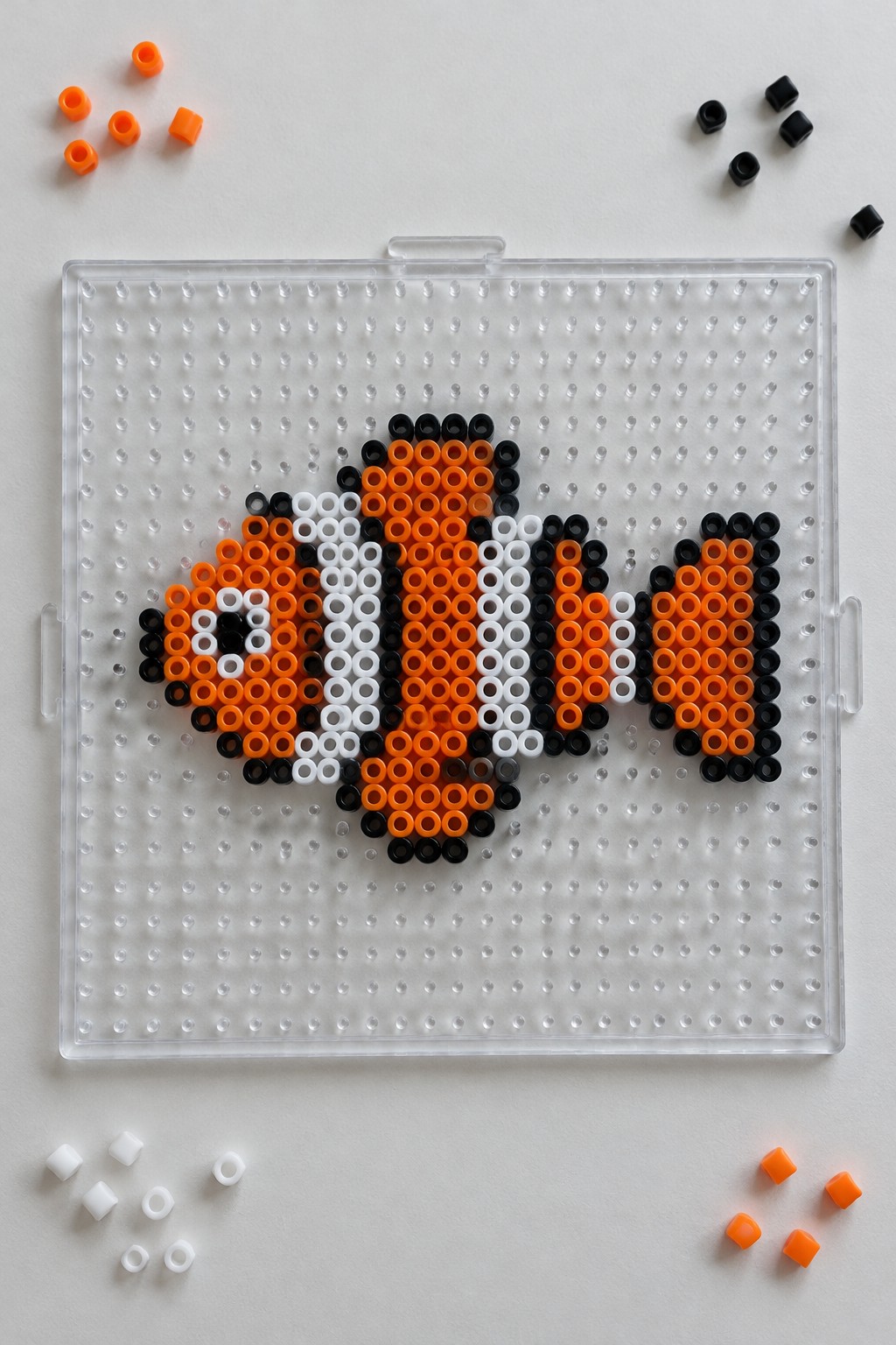 Clownfish Perler bead pattern in orange, white, and black on a pegboard.