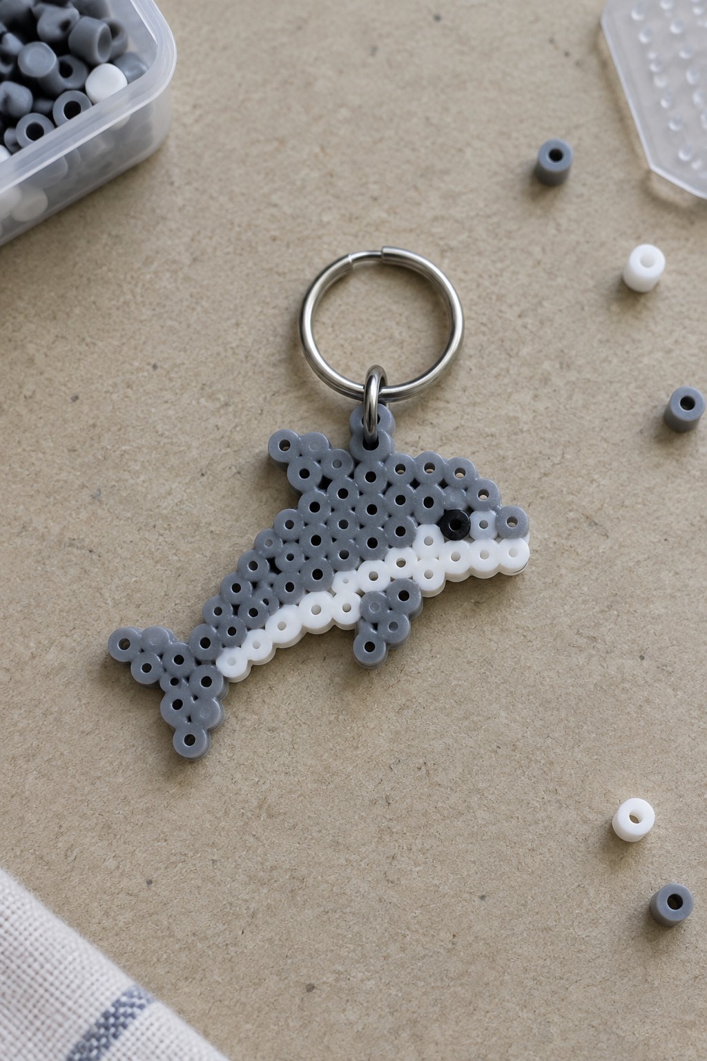 A fused Perler bead dolphin keychain in gray and white with a black eye, attached to a metal ring.