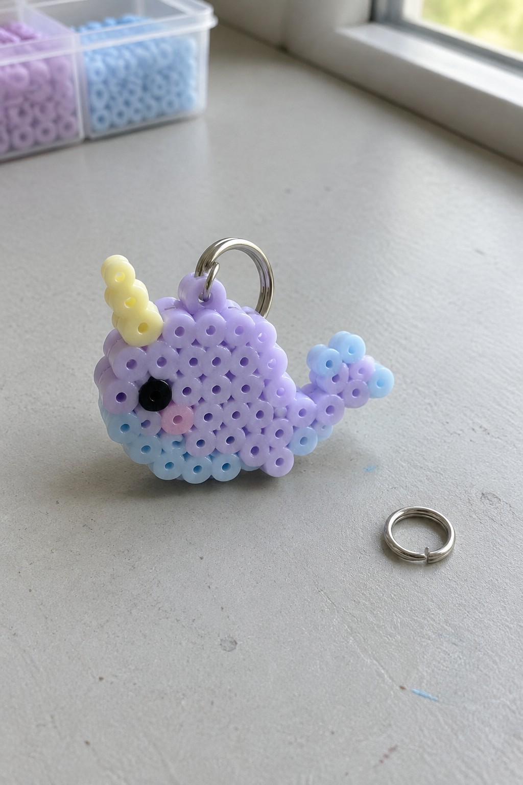 Purple beaded narwhal keychain with yellow horn beside loose silver ring