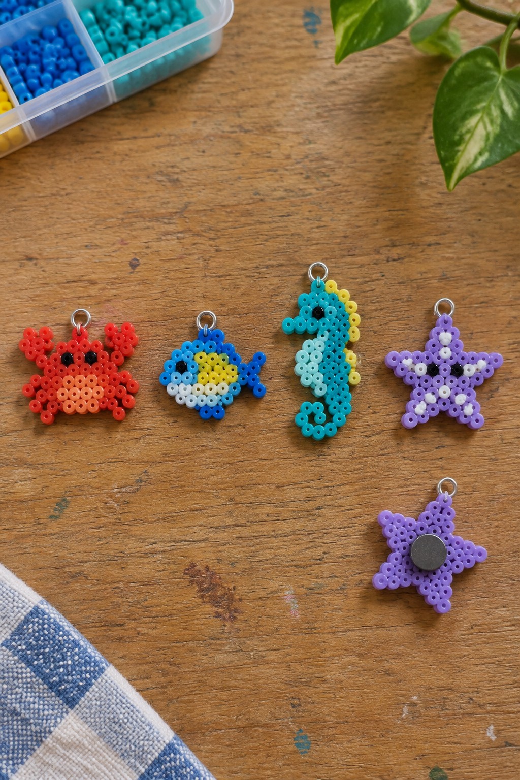 Colorful perler bead sea creatures—crab, fish, seahorse, starfish—on wooden table with beads