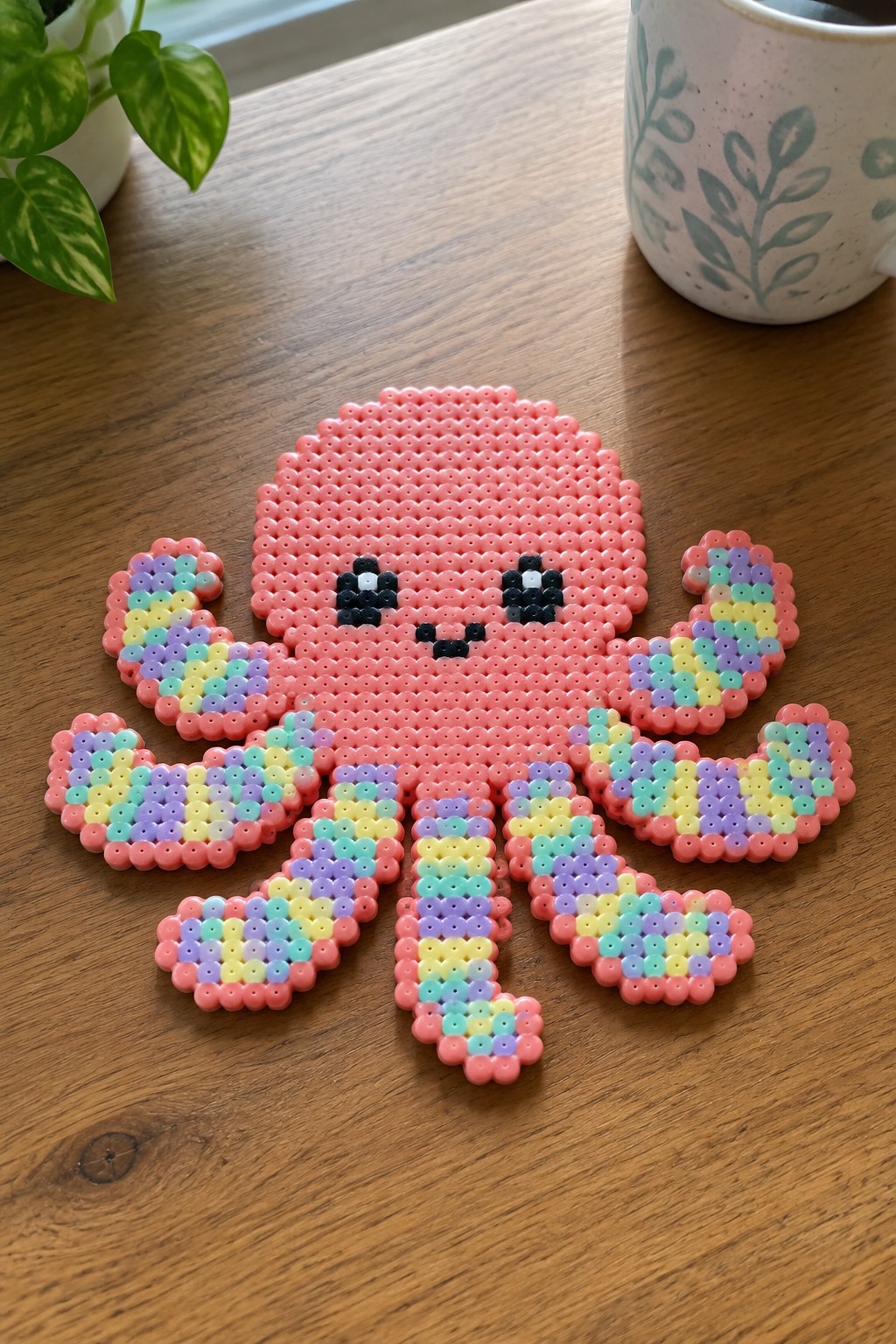 Pink perler bead octopus with rainbow tentacles and cute face on wooden table
