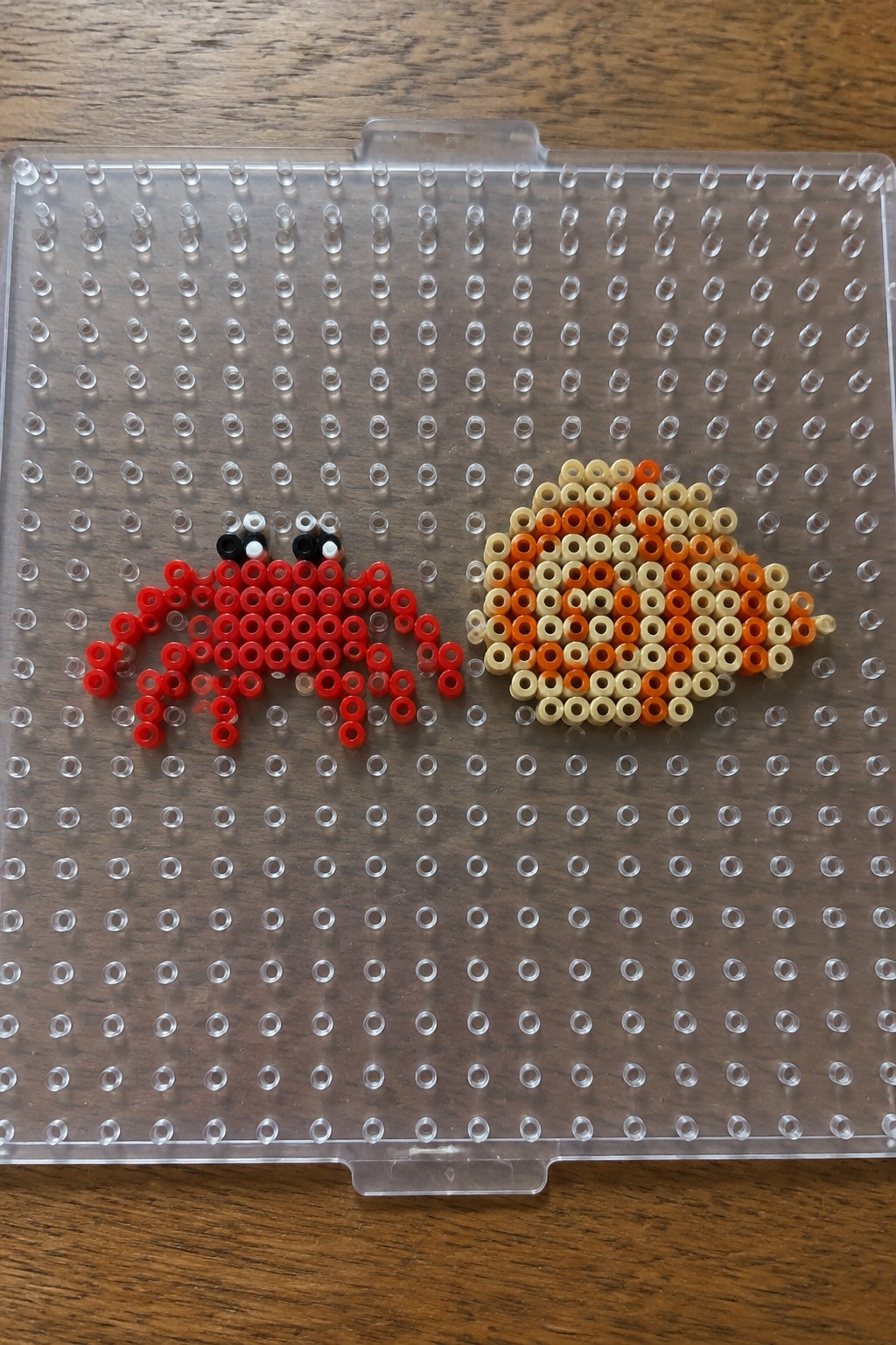 Red crab and orange fish Perler bead art on clear pegboard over wood