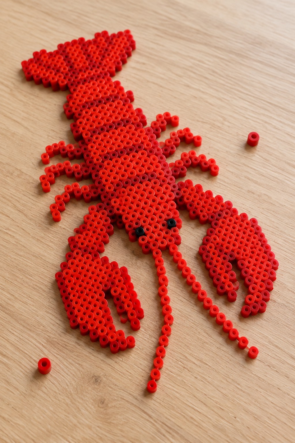 Red Perler bead lobster with black eyes arranged on a pegboard.