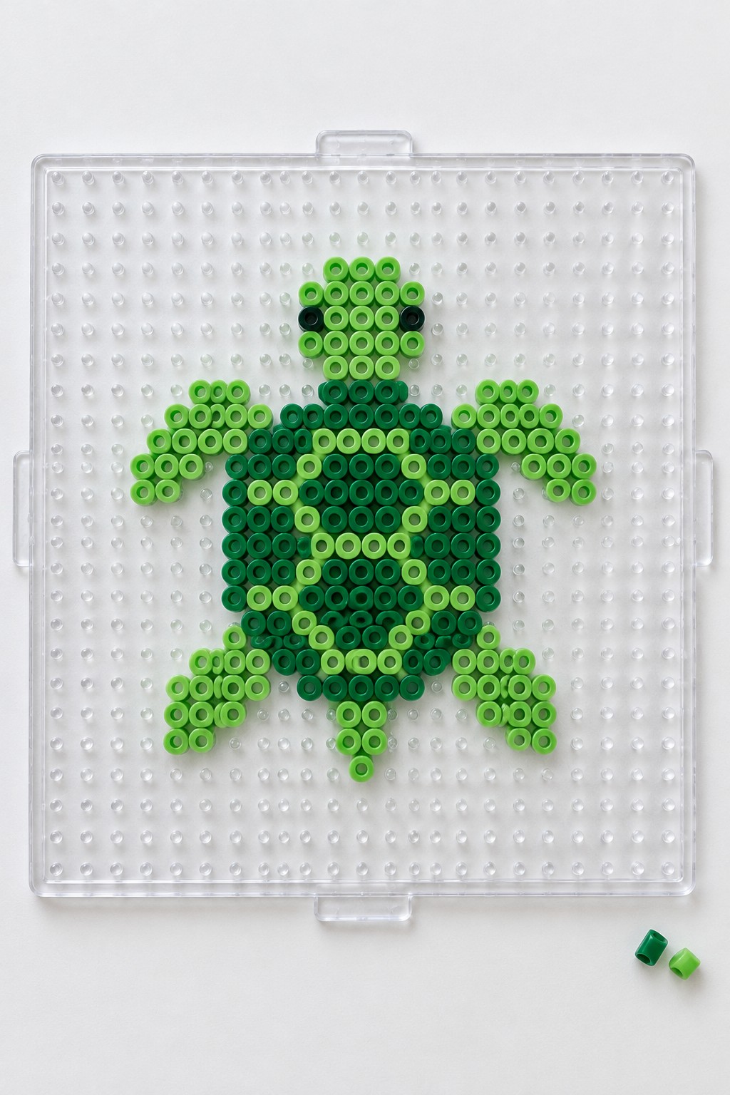 Sea turtle Perler bead pattern in multiple shades of green on a pegboard with black beads for eyes.