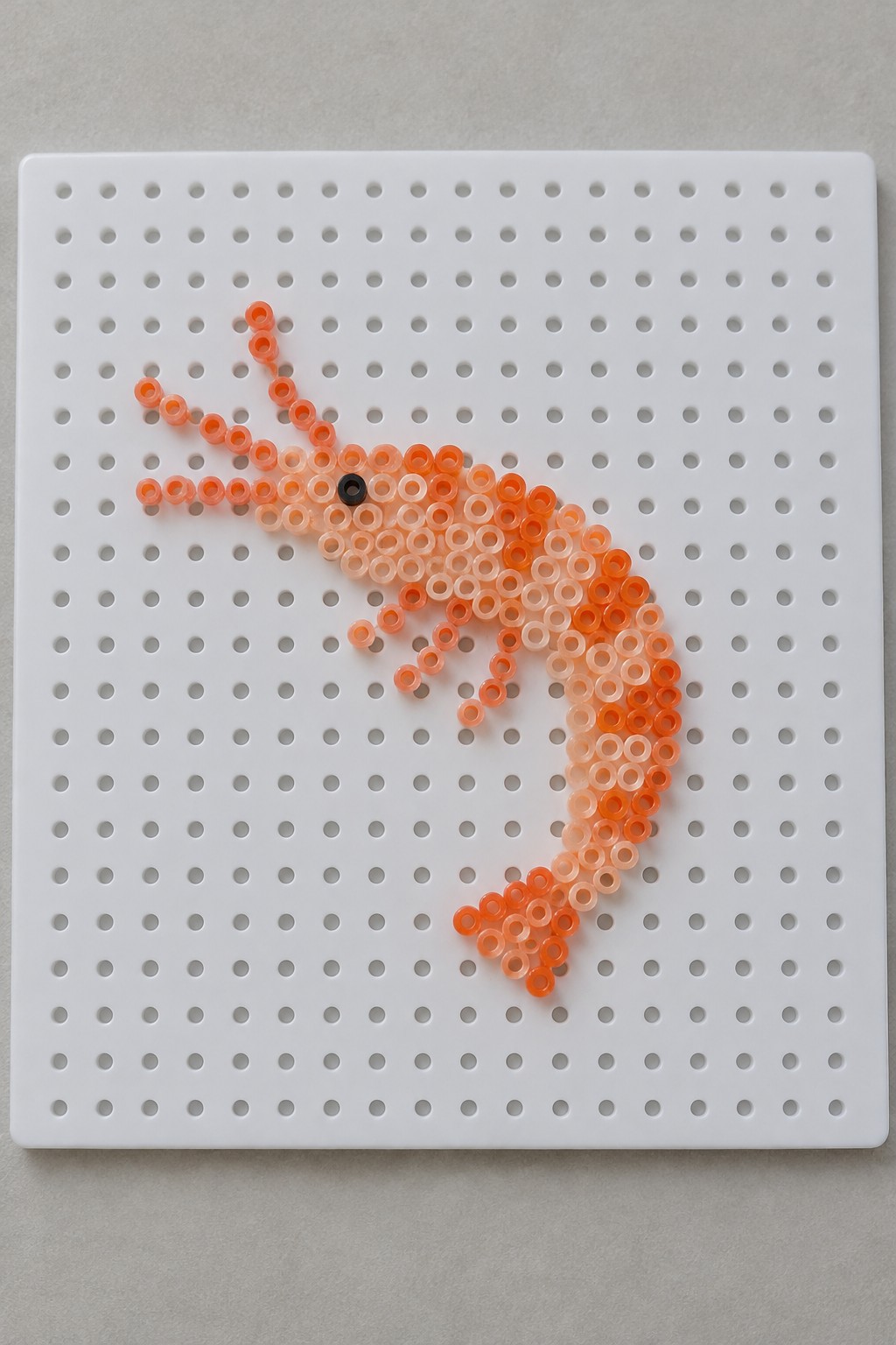 A Perler bead shrimp made with orange beads on a white pegboard.