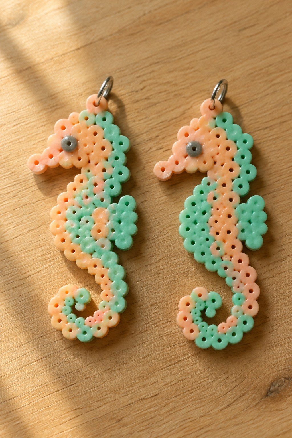 Two fused Perler bead seahorses in peach and mint green with metal jump rings at the top.