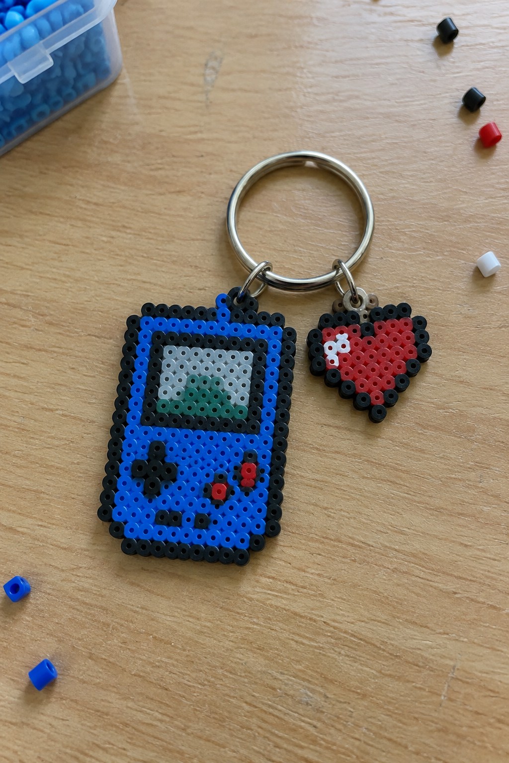 Blue perler bead Game Boy keychain with red heart charm on wood table