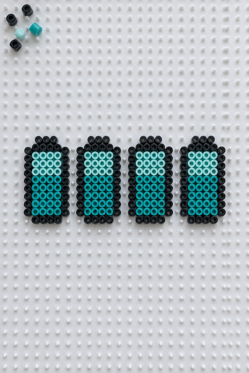 Four fuse-bead batteries in black and teal on white pegboard with loose beads nearby.