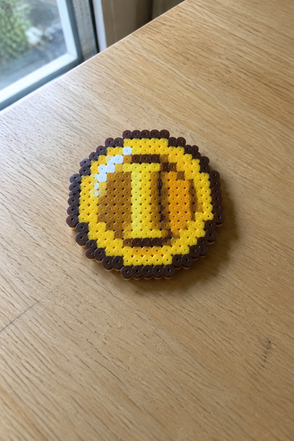 Perler bead art of yellow bee with brown stripes on wooden table