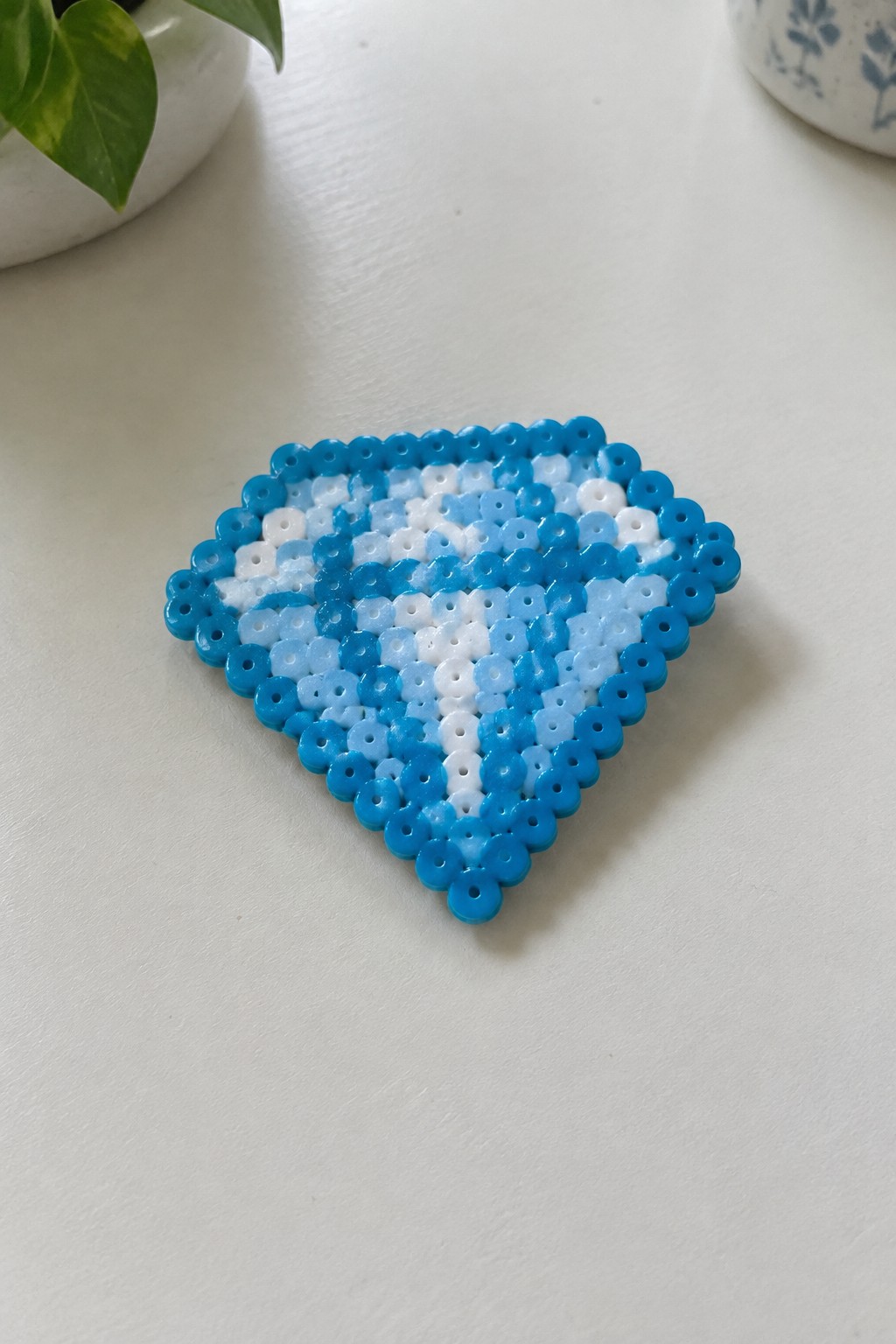 Blue and white beaded diamond craft on white surface with potted plants nearby.