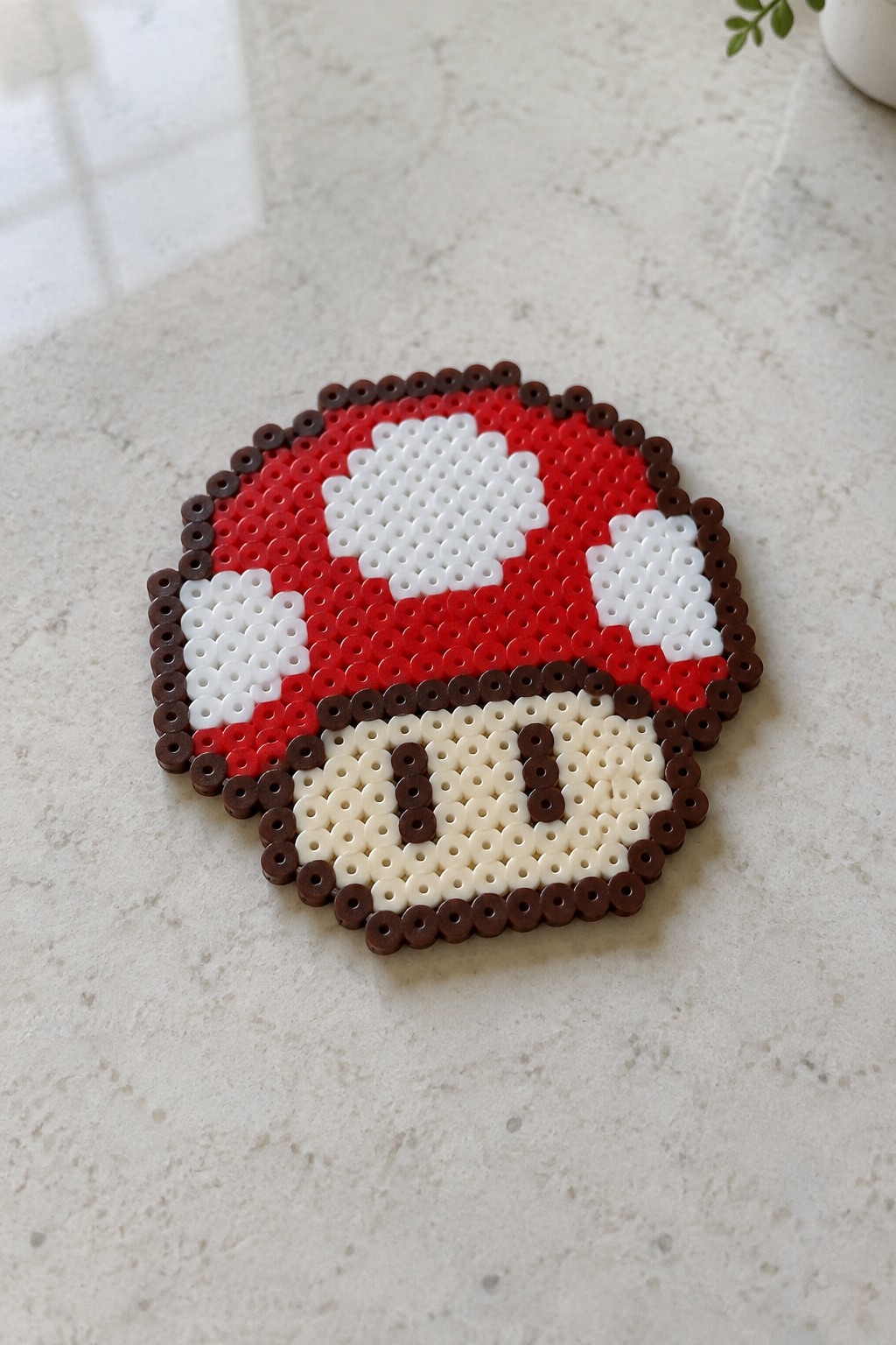 Perler beads on a pegboard forming a red mushroom sprite with white spots, brown border, and beige base with eyes.