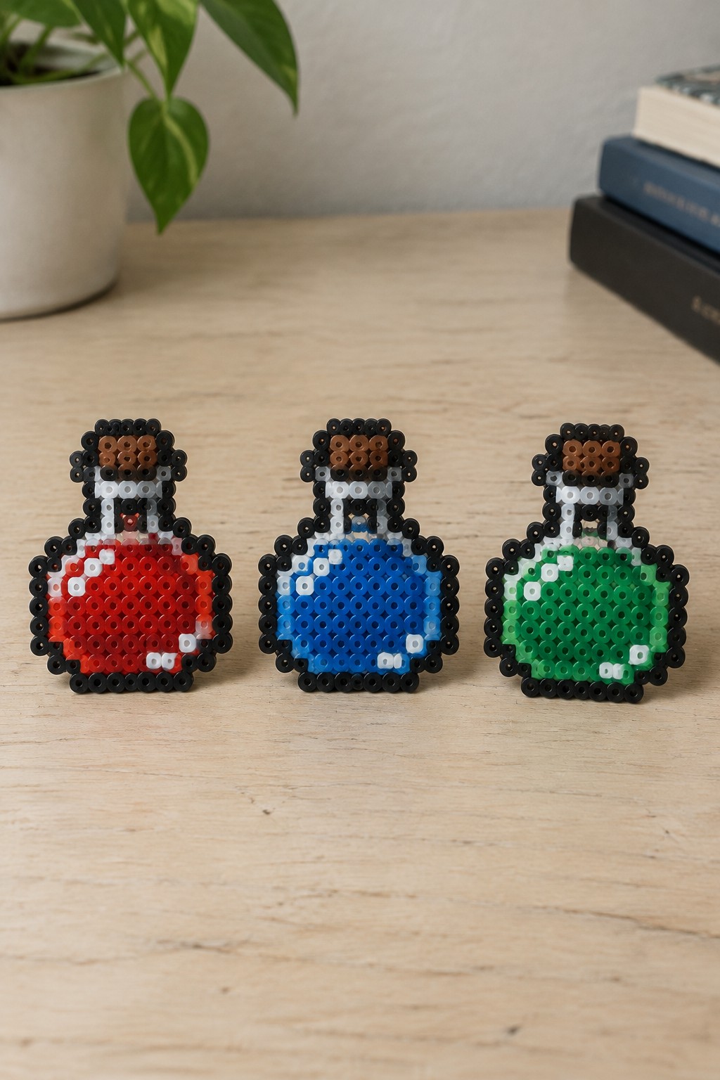 Three Perler bead potion bottle patterns in red, blue, and green with black outlines and simple faces.
