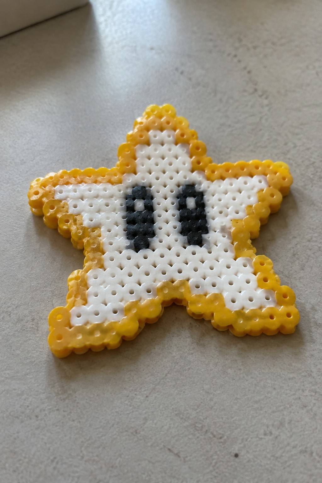 Yellow and white perler bead star with black eyes on a table.
