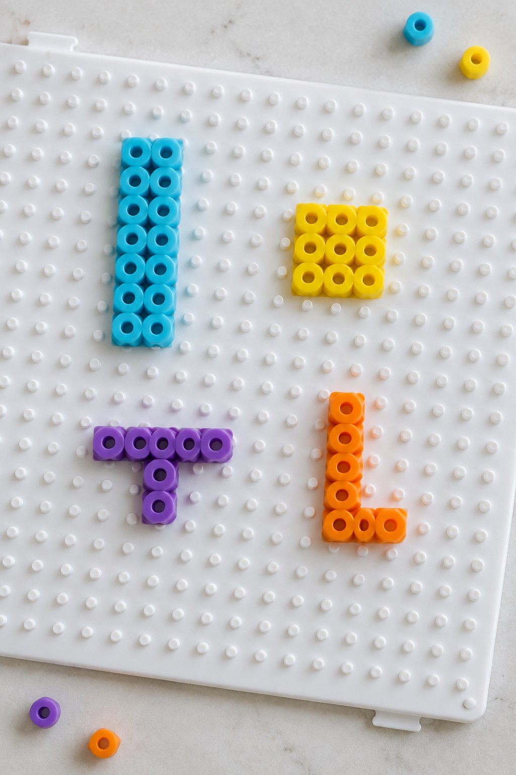 Beads forming blue I, yellow square, purple T, orange L on white pegboard