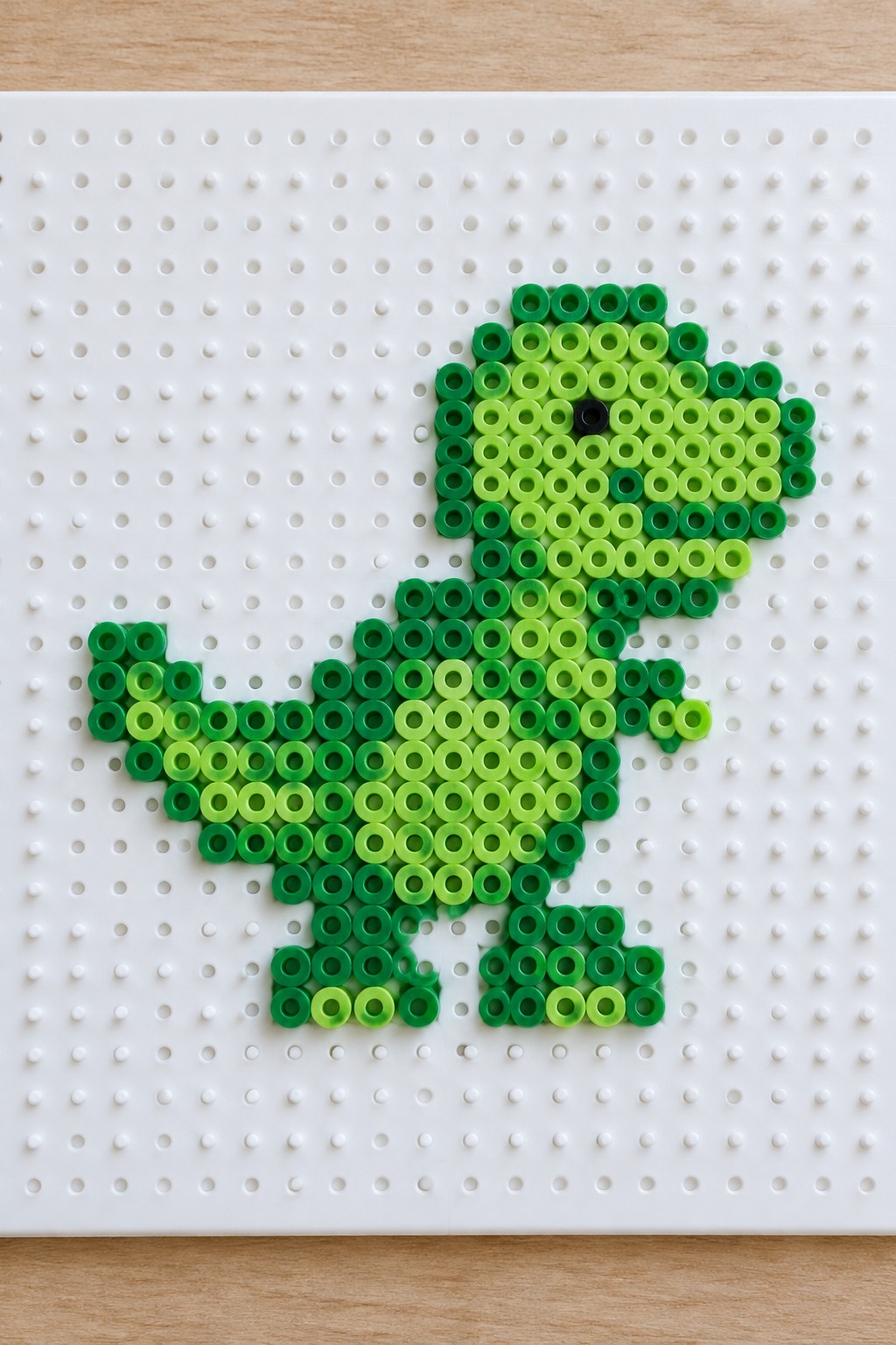 Green gradient beads forming dinosaur on white pegboard craft board