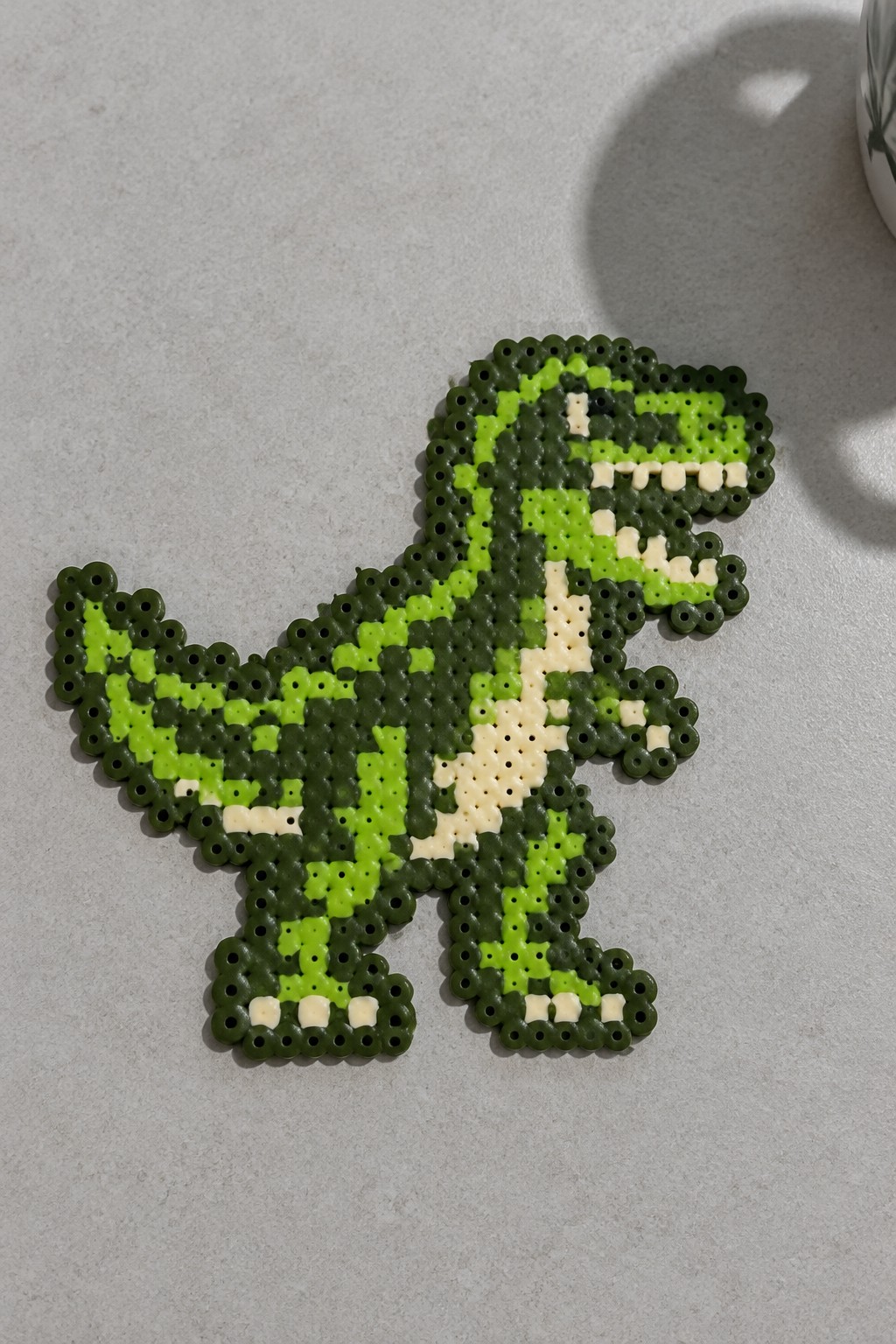 Green pixelated T-Rex dinosaur made from green and white perler beads.