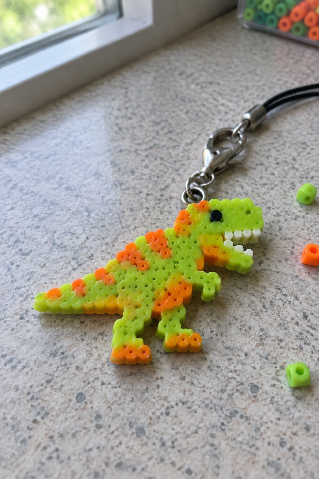 Green-orange perler bead T-rex keychain with metal clasp on speckled countertop