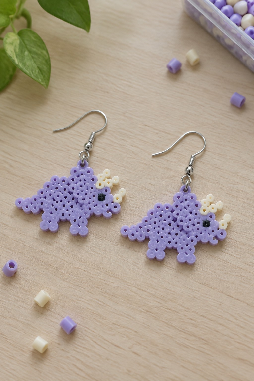 Purple perler bead dinosaur earrings with white accents on wooden table