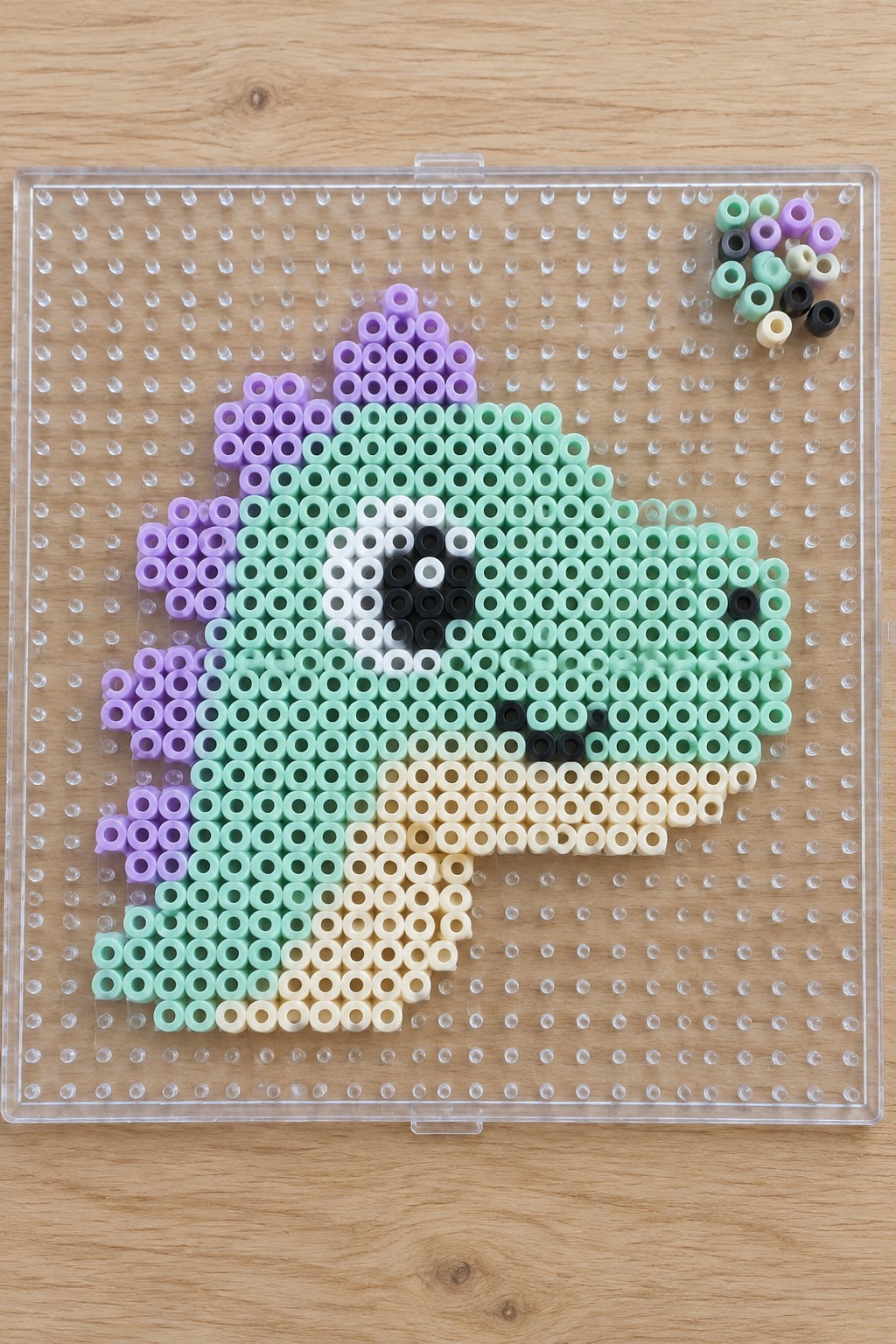 Perler beads forming a cute cat on a clear pegboard with loose beads aside.