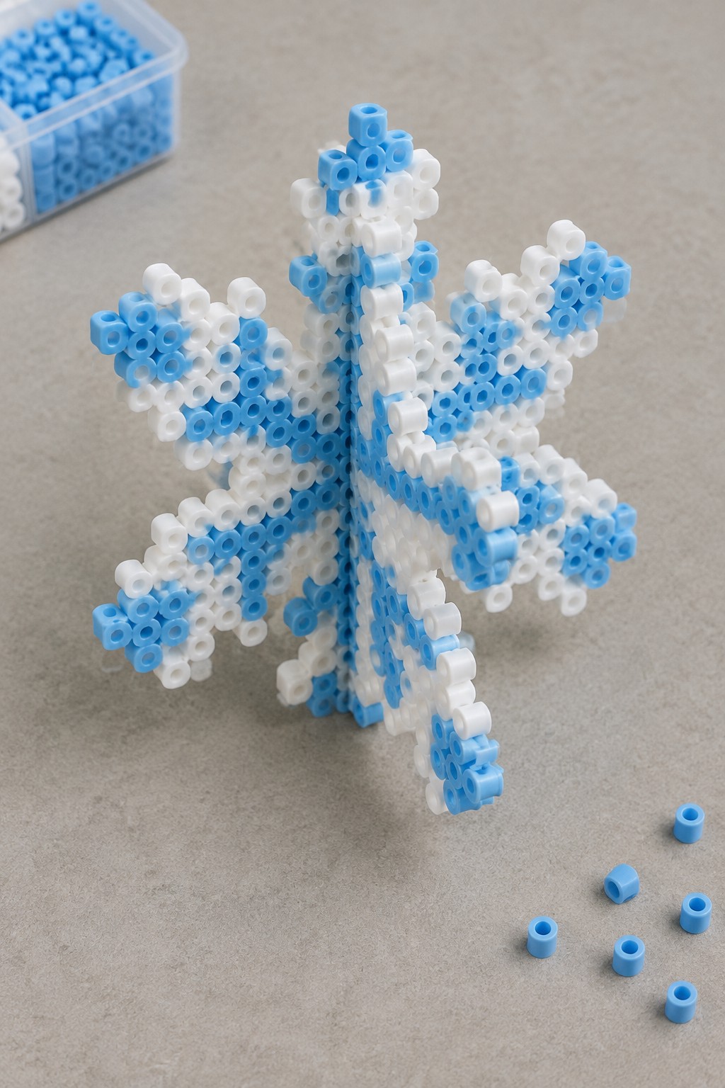 White and blue perler bead snowflake on gray surface with loose beads nearby
