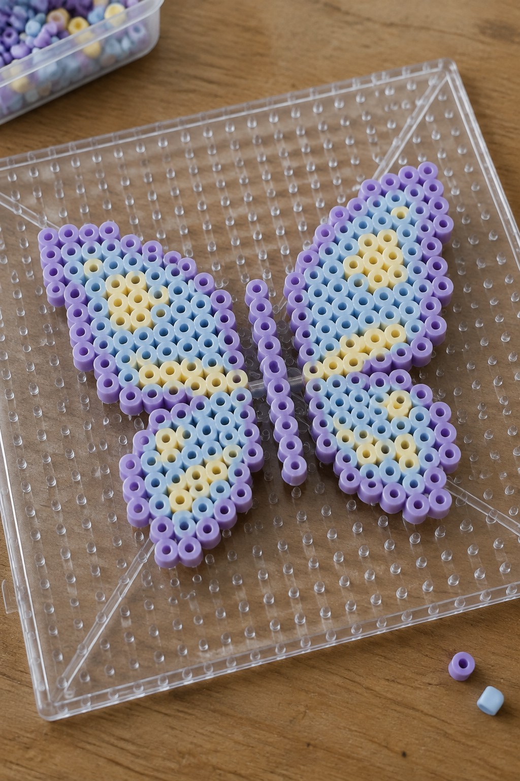 Two pastel butterfly perler bead designs on clear pegboard over wood