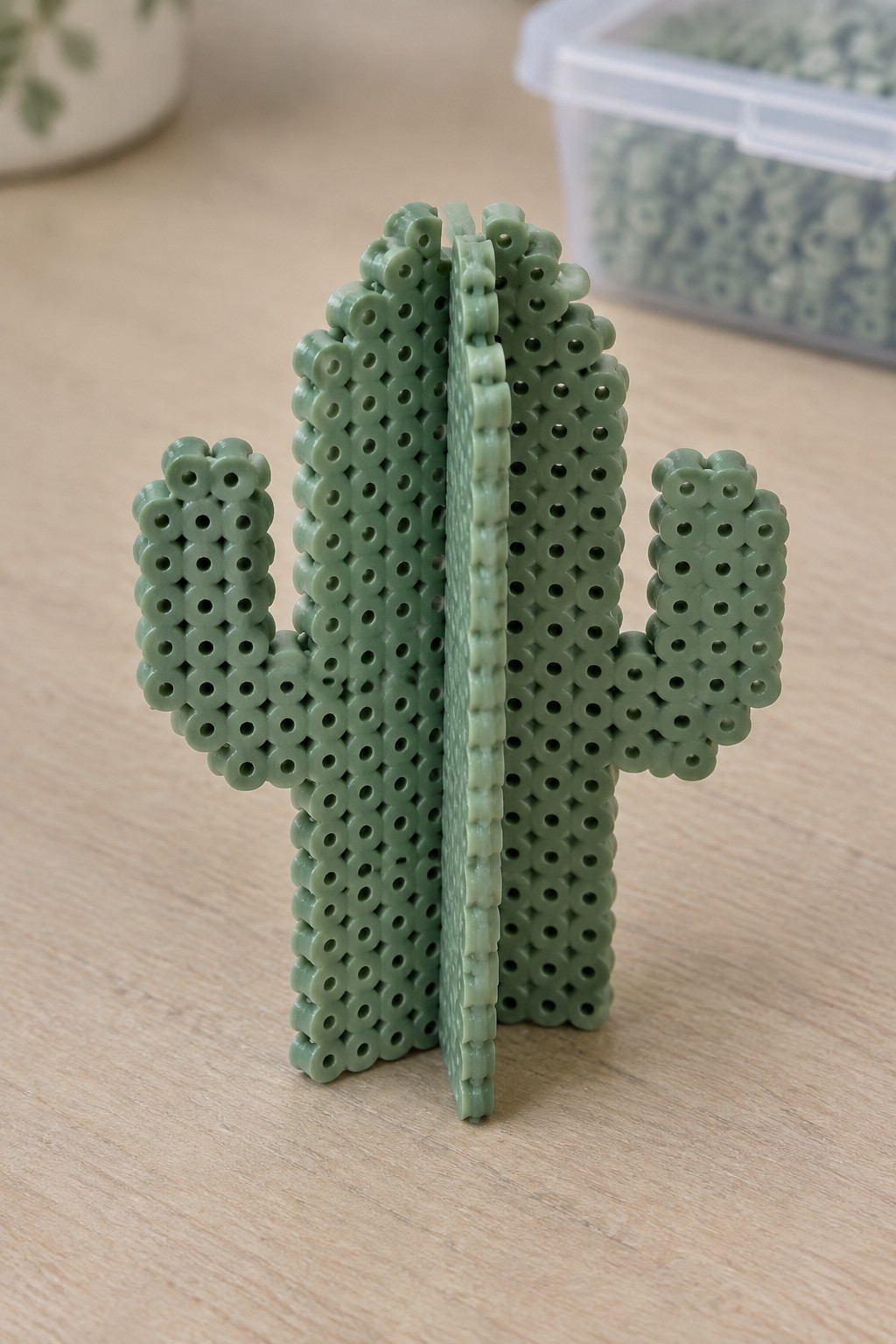 Green Perler bead saguaro cactus with arms on wooden table, beads in background