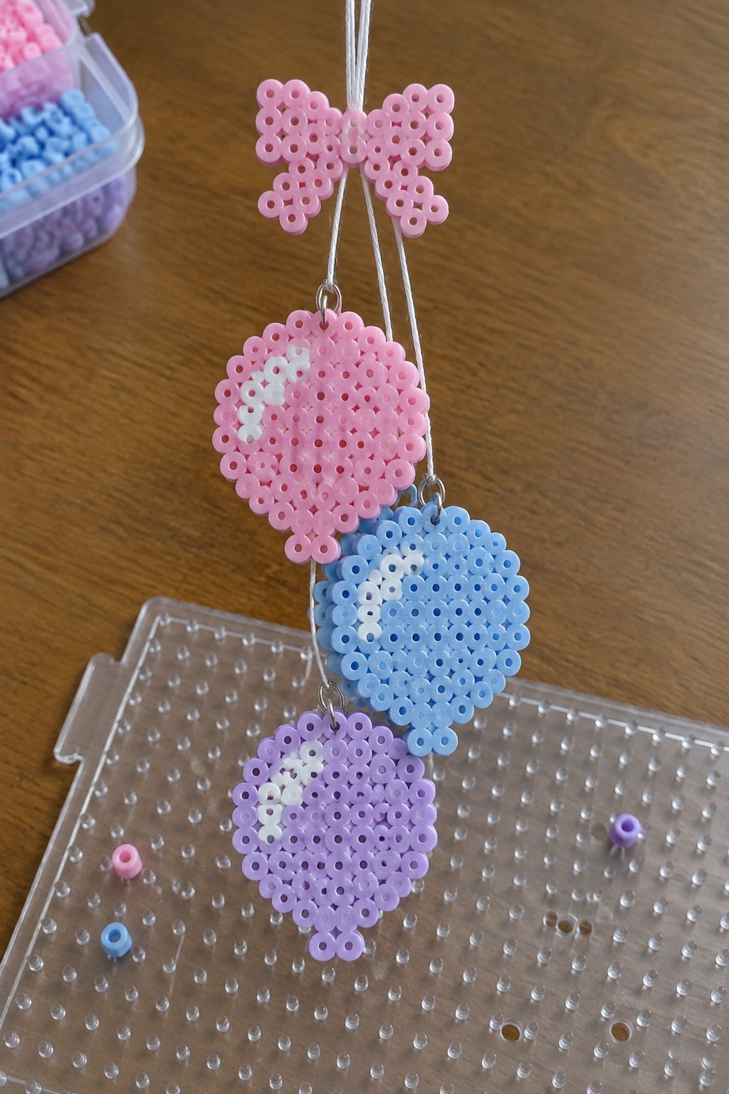 Three perler bead hearts in pink, blue, and purple hanging from a bow