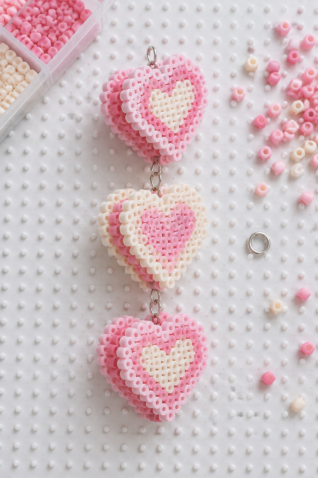Three linked pink-and-white perler-bead hearts with scattered beads and storage box