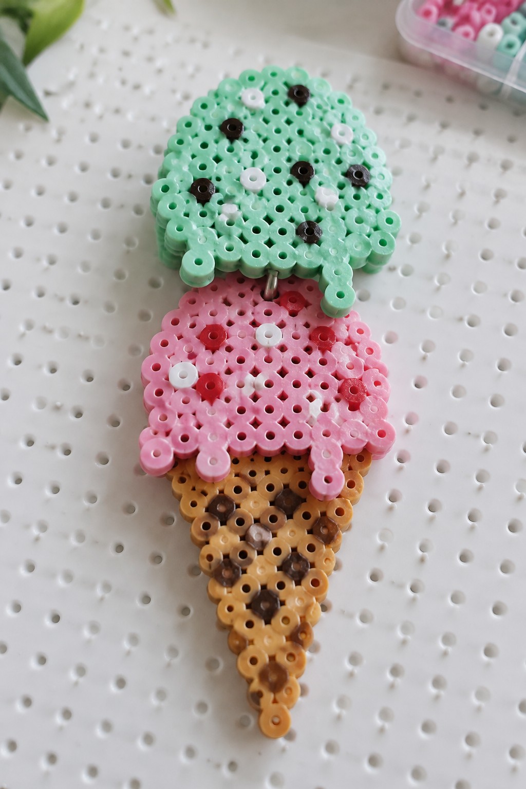 Mint green and pink perler bead ice cream cone on white pegboard.
