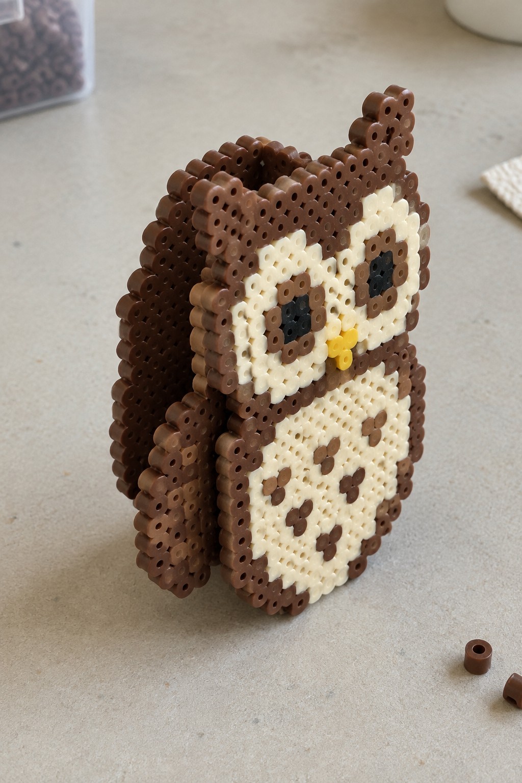 Perler bead owl with brown body, cream face, black eyes, and yellow beak