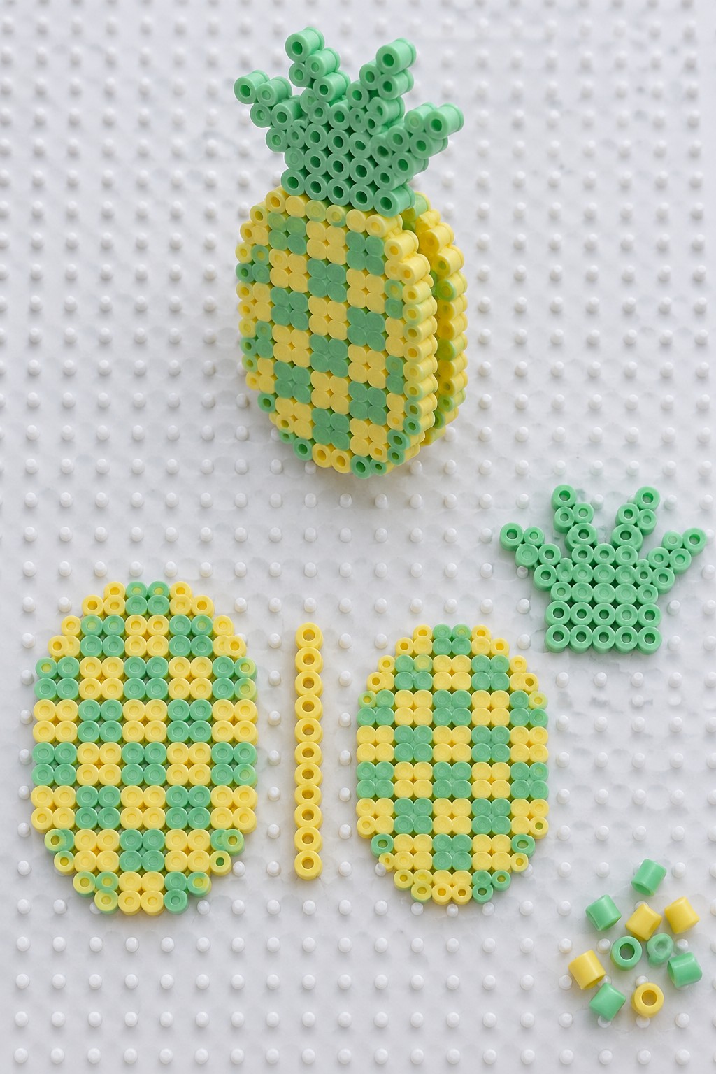 3D Perler bead pineapple assembled from yellow and green layered panels, shown with separate flat body and crown pieces on a pegboard.