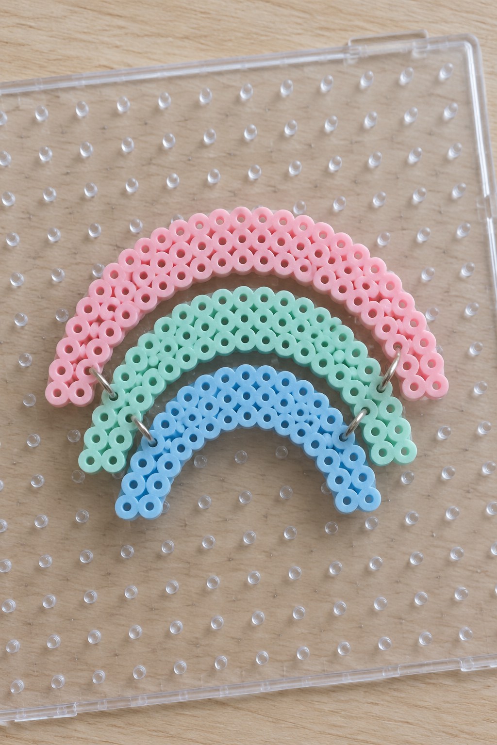 Pink, mint green, and blue perler bead rainbow on clear pegboard with rings