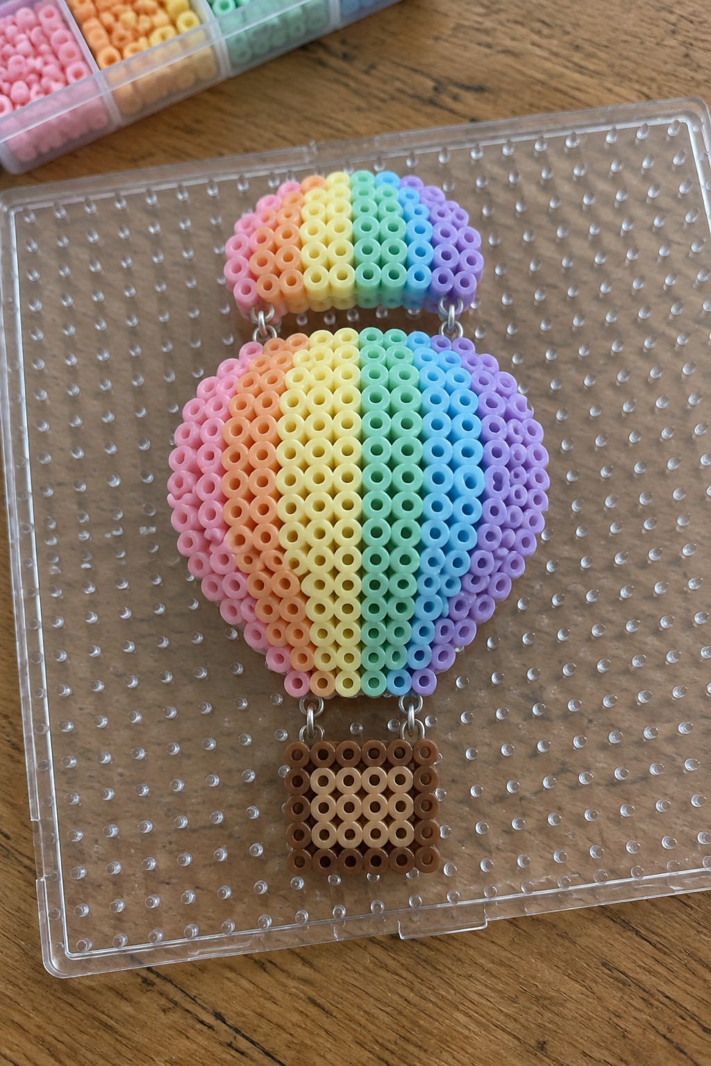 Rainbow perler bead hot air balloon with brown basket on pegboard