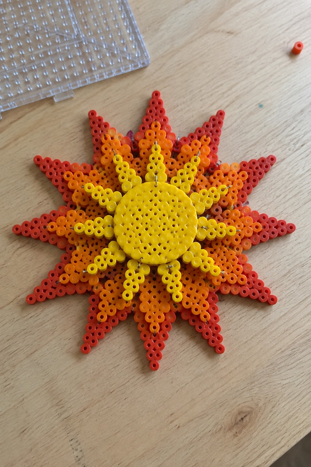 Perler bead sun with yellow center and gradient red-orange rays on wood table
