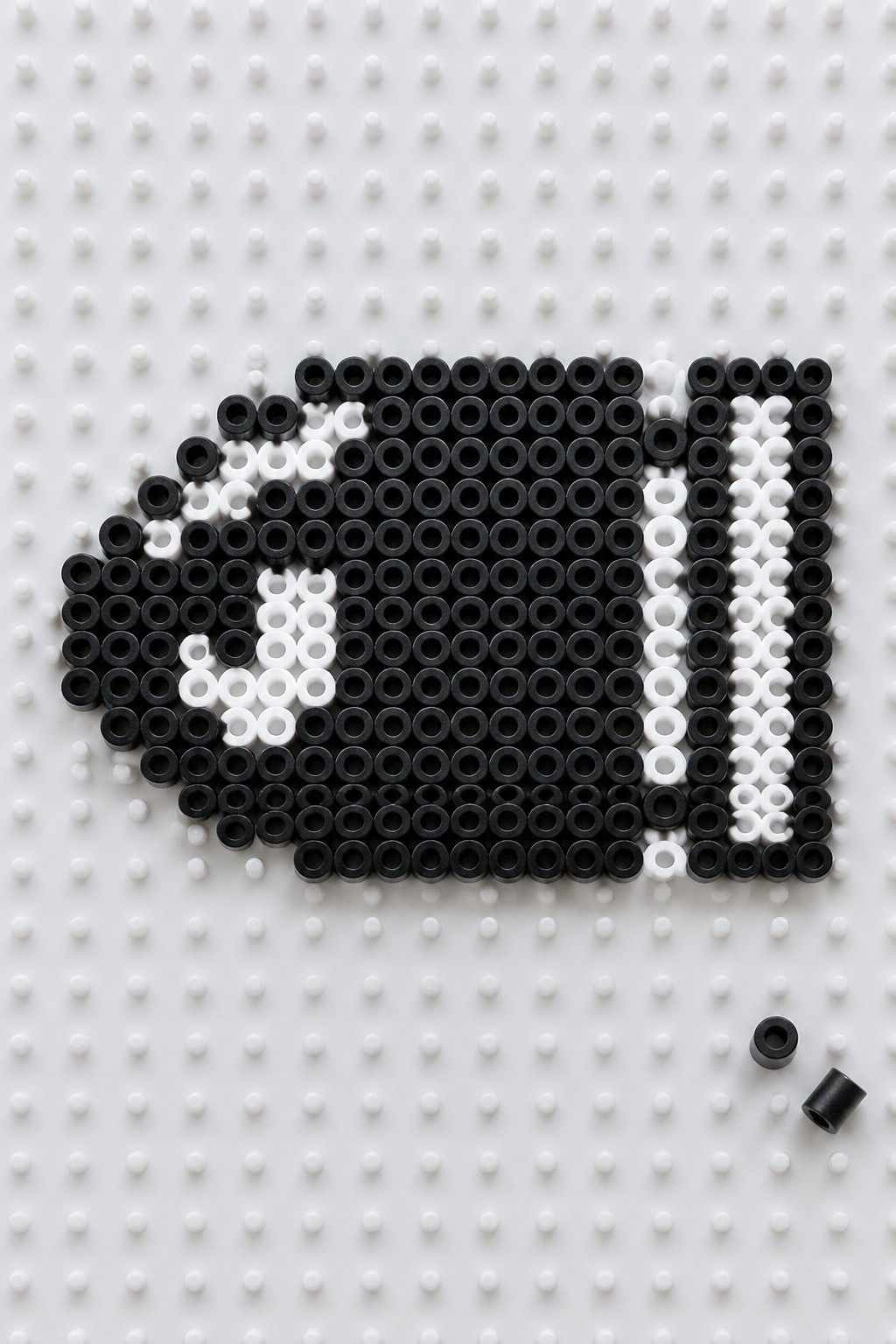 Black and white Perler beads forming a Bullet Bill on a white pegboard.