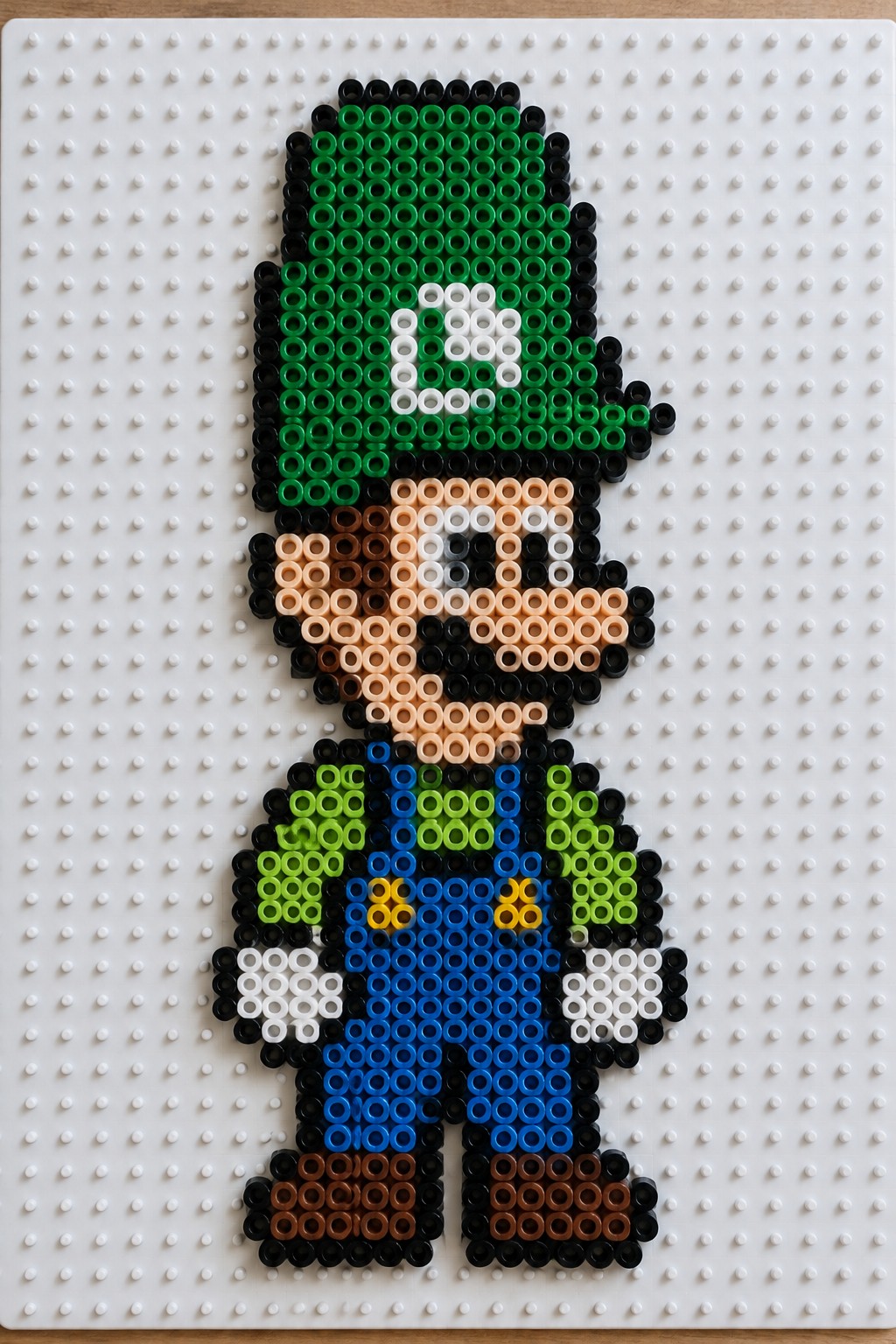 Luigi bead figure with green hat and blue overalls on white pegboard