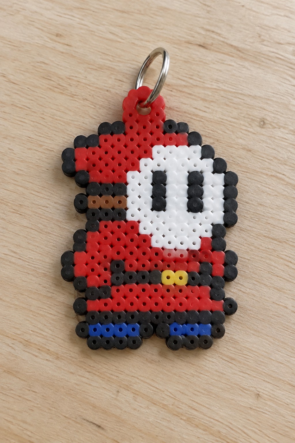 Perler bead keychain of red pixel character with white face, black eyes and blue shoes