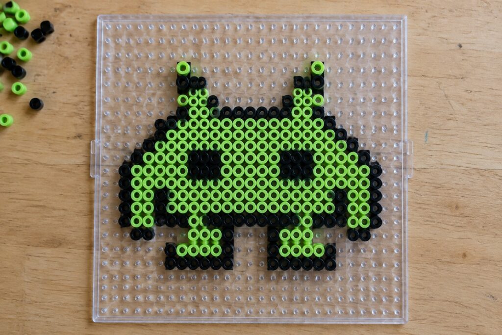 22 Retro Video-Game Character Perler Bead Patterns Neon green and black perler beads forming a cat on a clear pegboard