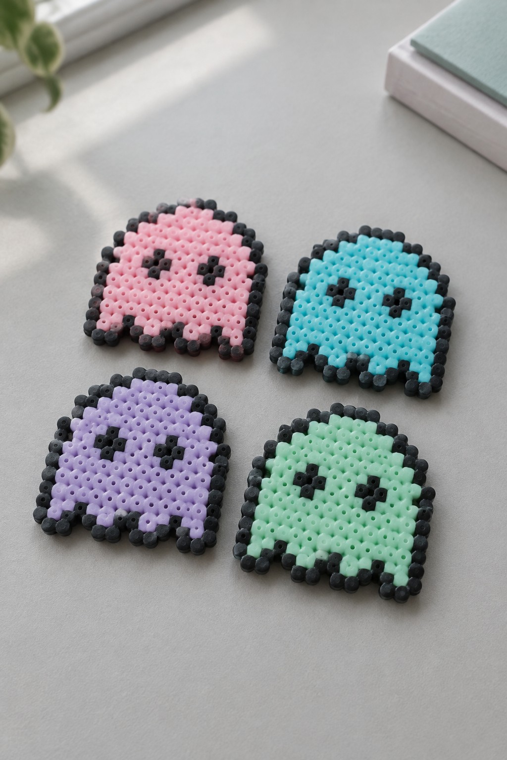 Four perler bead ghosts in pink, blue, purple, and mint green.