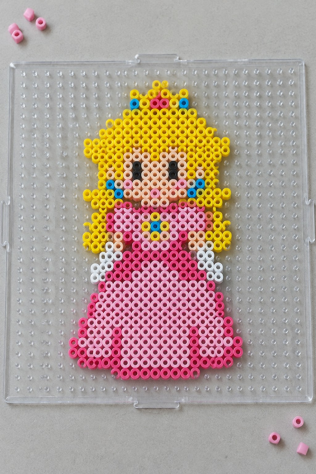 Princess Peach perler bead art with yellow hair and pink dress on pegboard.
