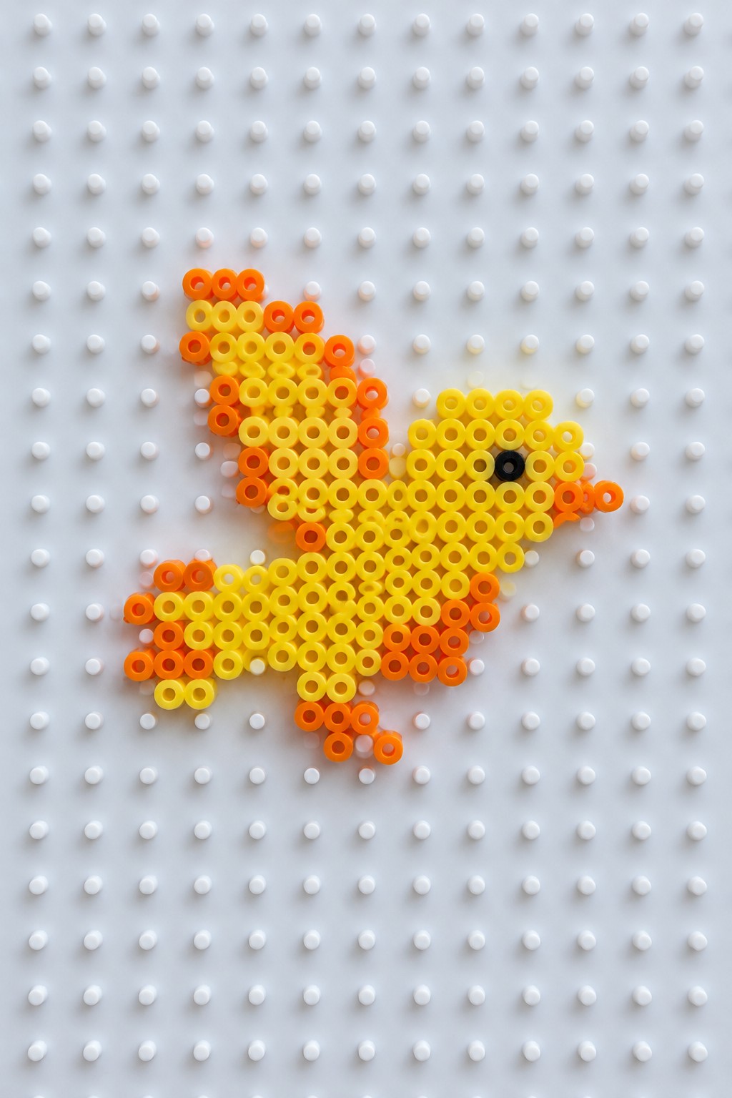 Yellow and orange perler bead bird with black eye on pegboard