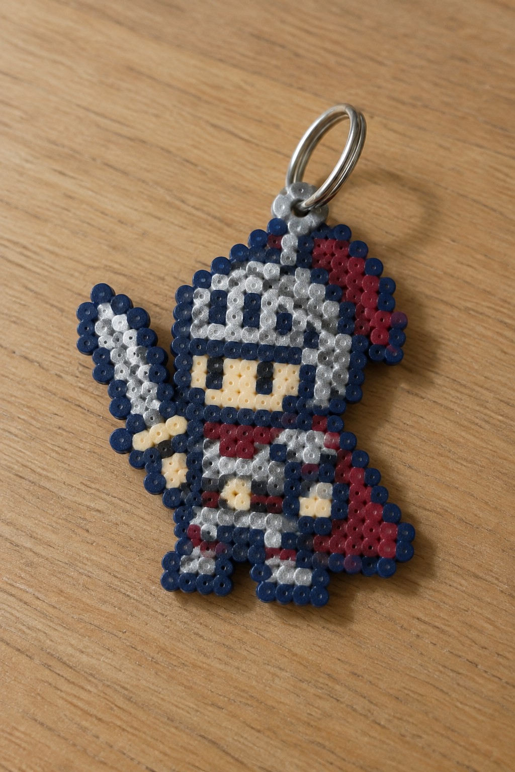 Perler bead pixel art keychain of helmeted blue-red character with metal ring on wood