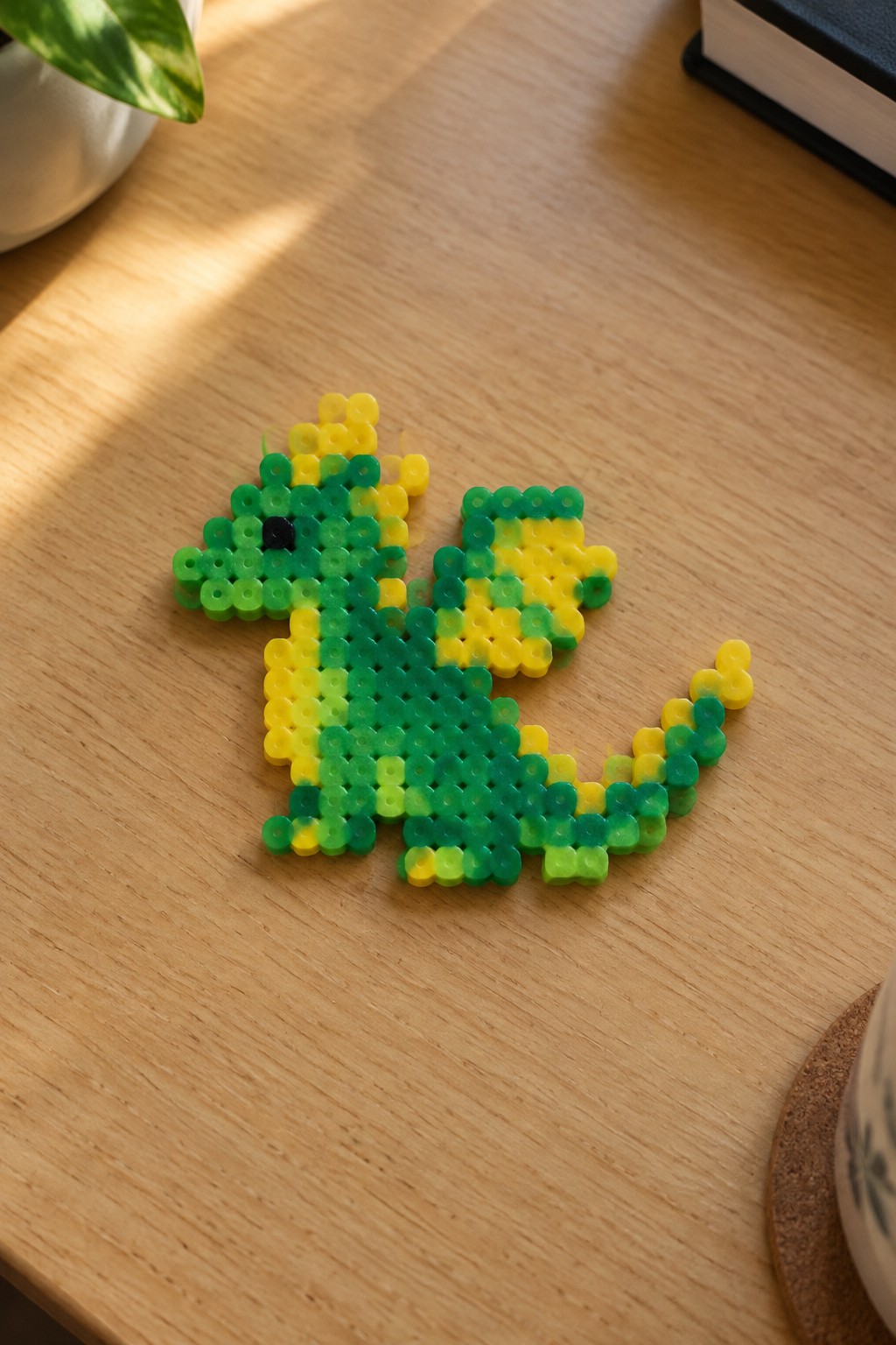 Green-yellow perler bead dragon with black eye on light wooden table
